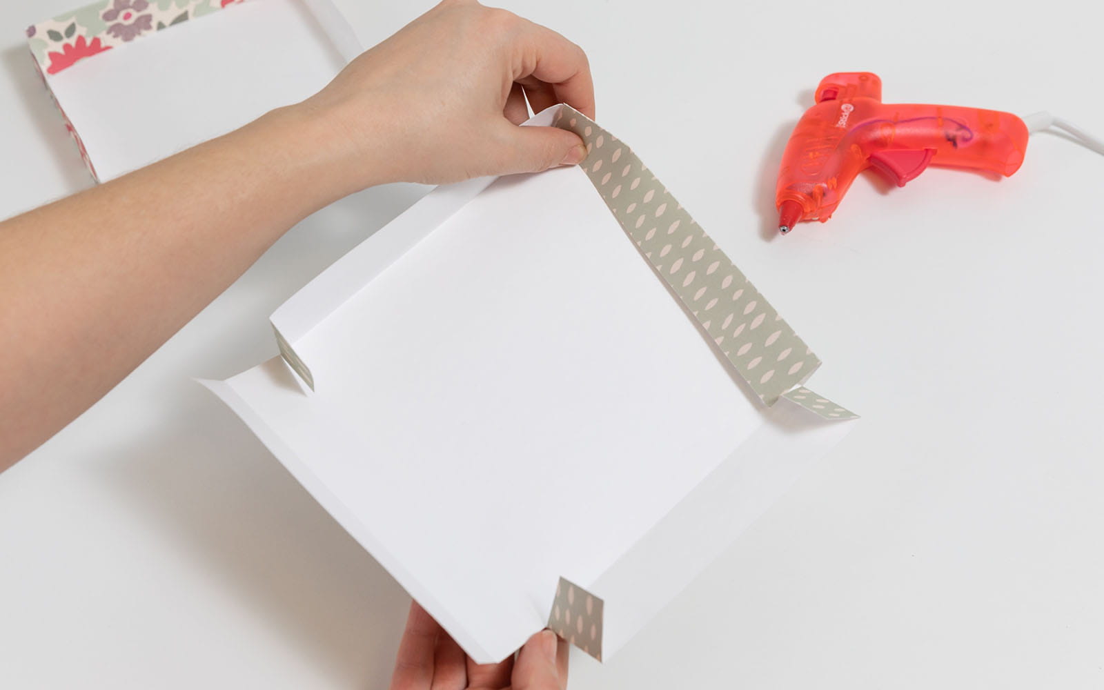 Hände die Deckel einer Papierbox mit Klebepistole zusammenkleben