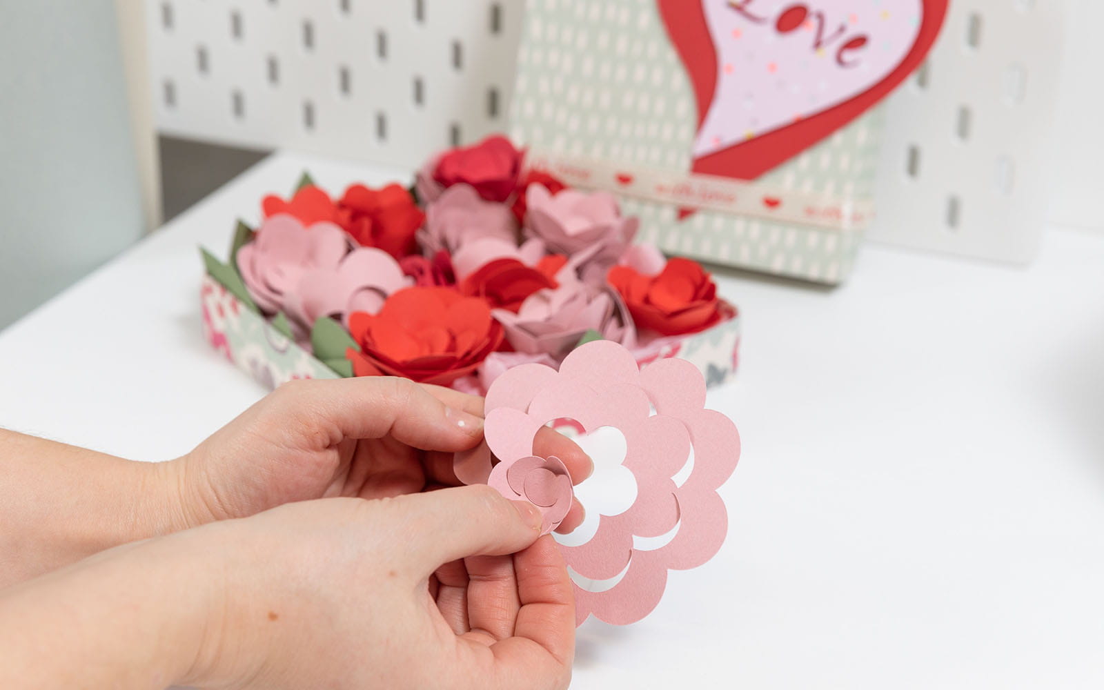 Hands holding pink papercraft spiral and turning into rose