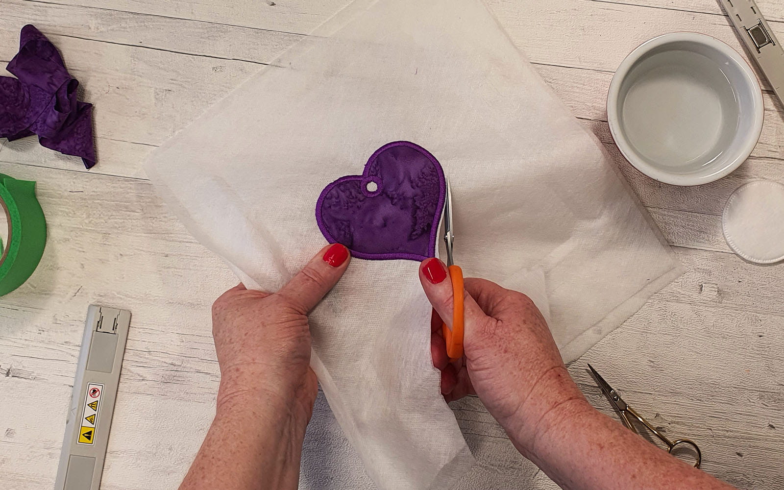 Scissors cutting purple heart from white fabric