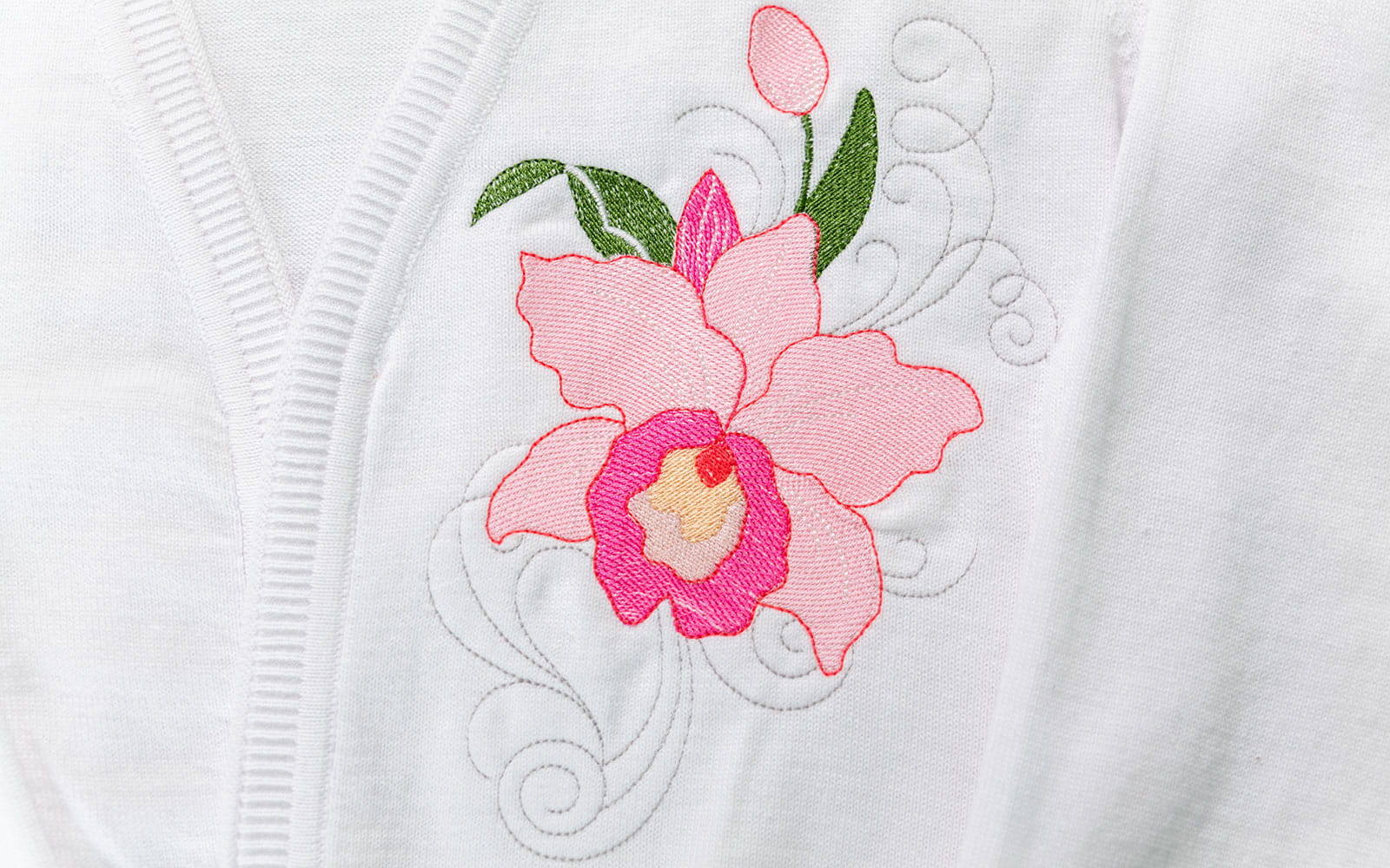 Nahaufnahme rosa Orchidee auf der Brust einer weißen Strickjacke gestickt