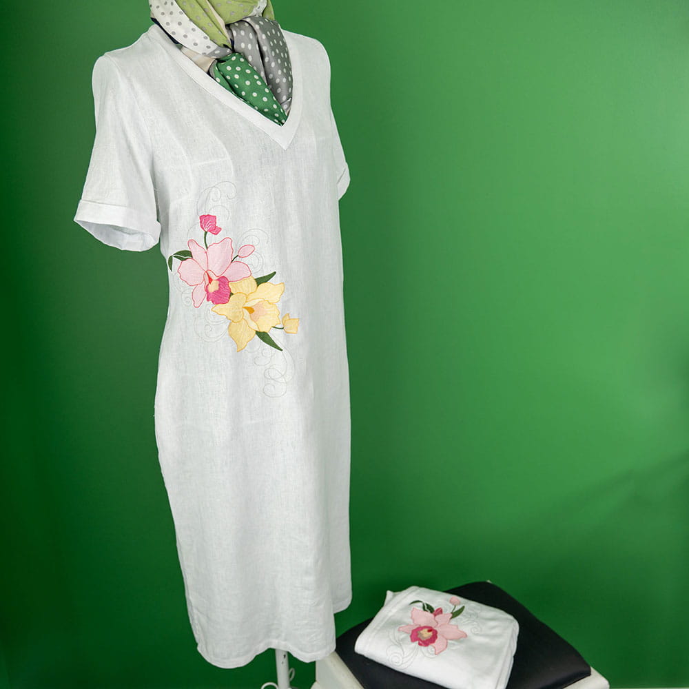 abito in lino con ricamo orchidea contro parete verde e cardigan abbinato