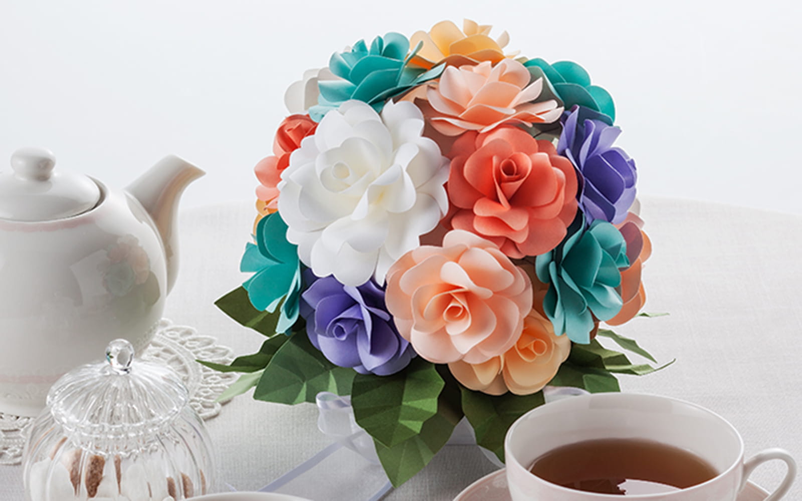 A bunch of pastel papercraft flowers on white table with tea set