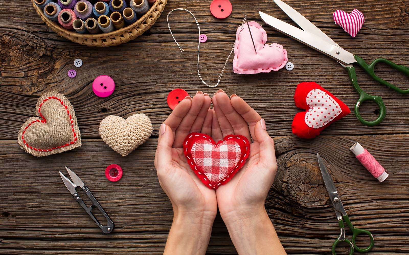 Patchwork red heart held in hands on wooden background