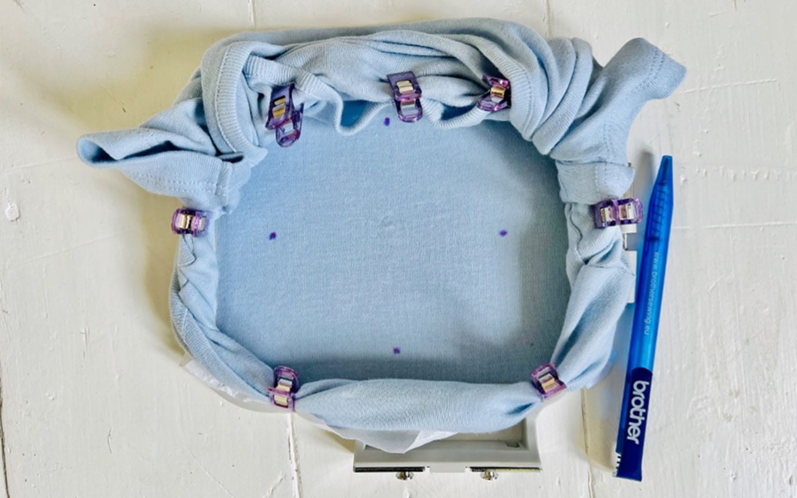 Blue babygrow rolled and clipped around a Brother embroidery hoop