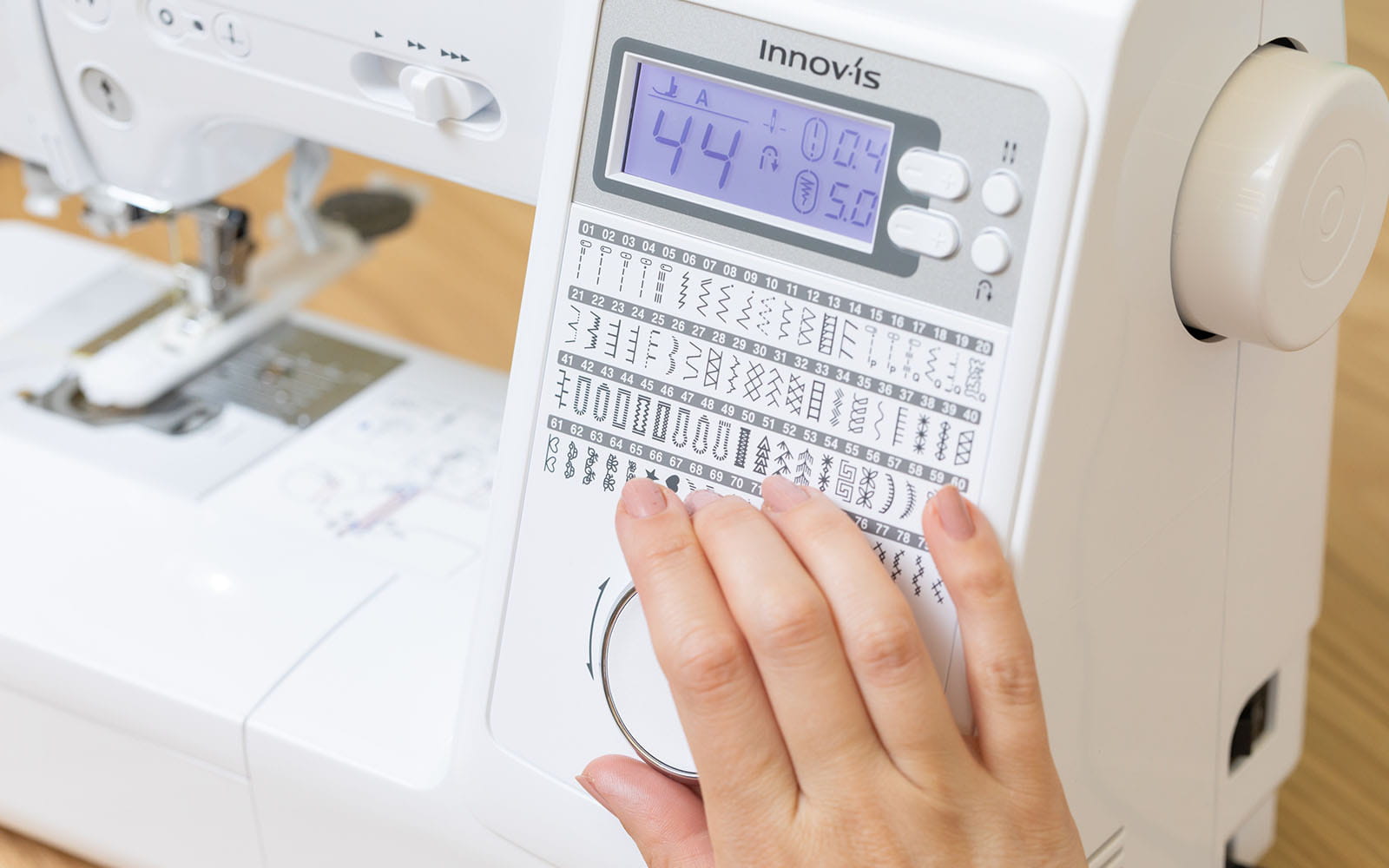Hand choosing stitch via dial on white Brother sewing machine 
