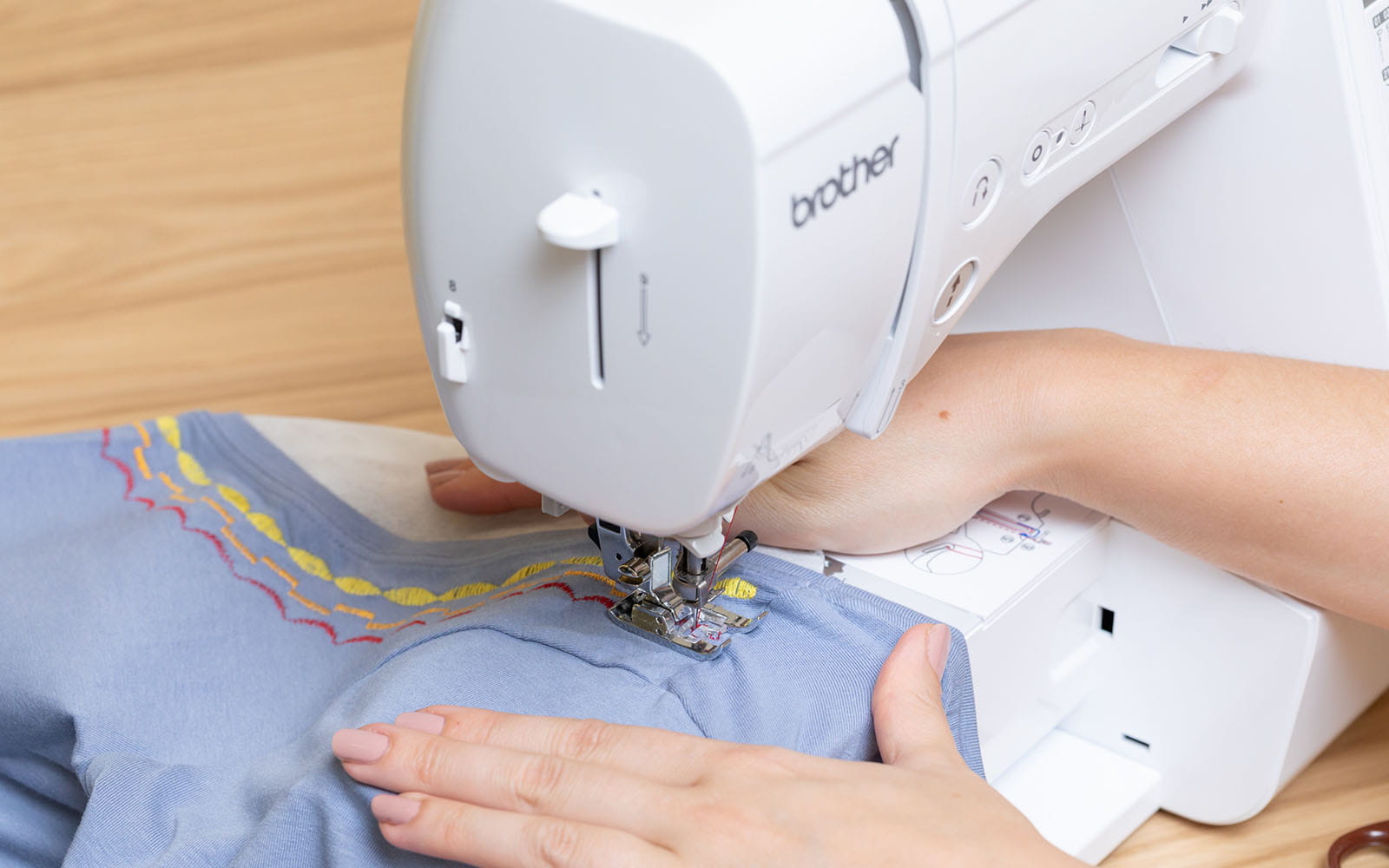 Hands sewing decorative stitching on neckline of blue T-shirt 