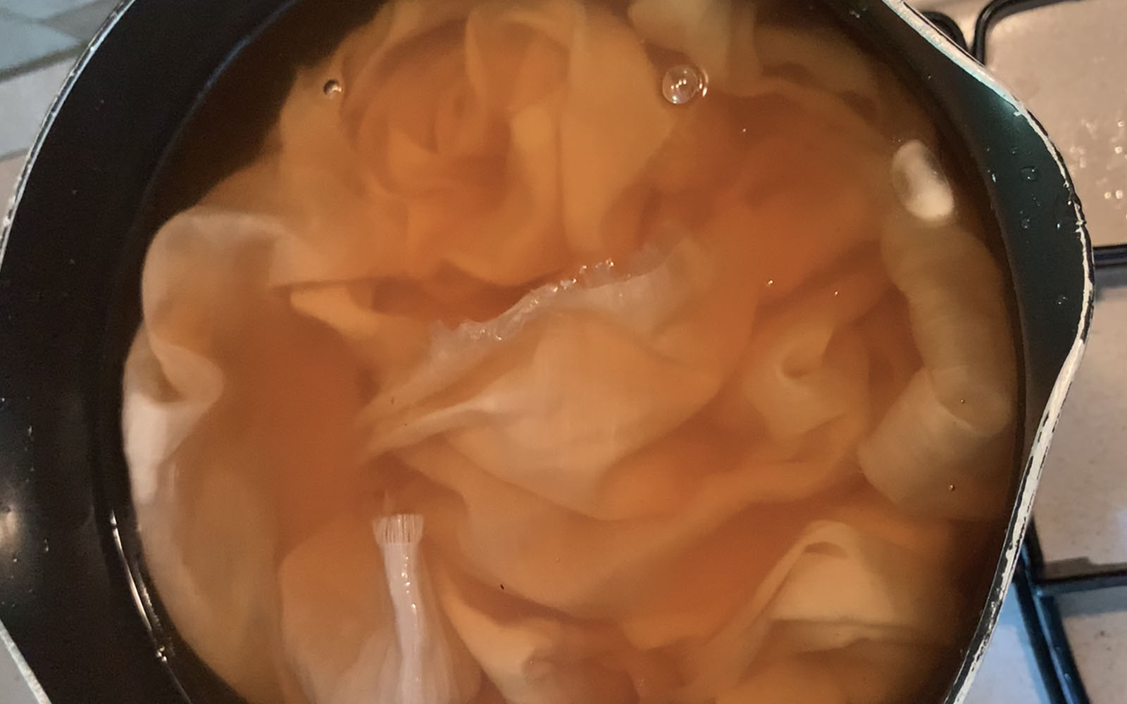 peach silk fabric submerged in avocado dye in cooking pan