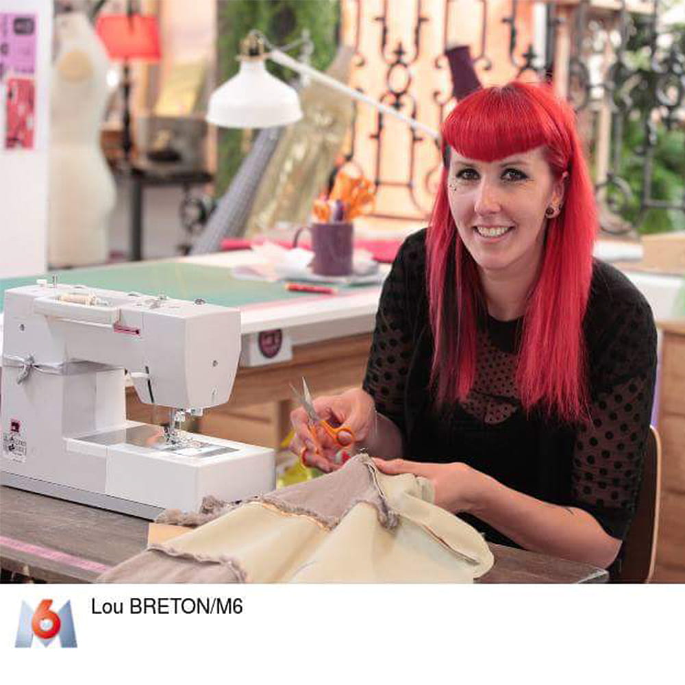 Oriane, a red haired woman, sits with a seam ripper