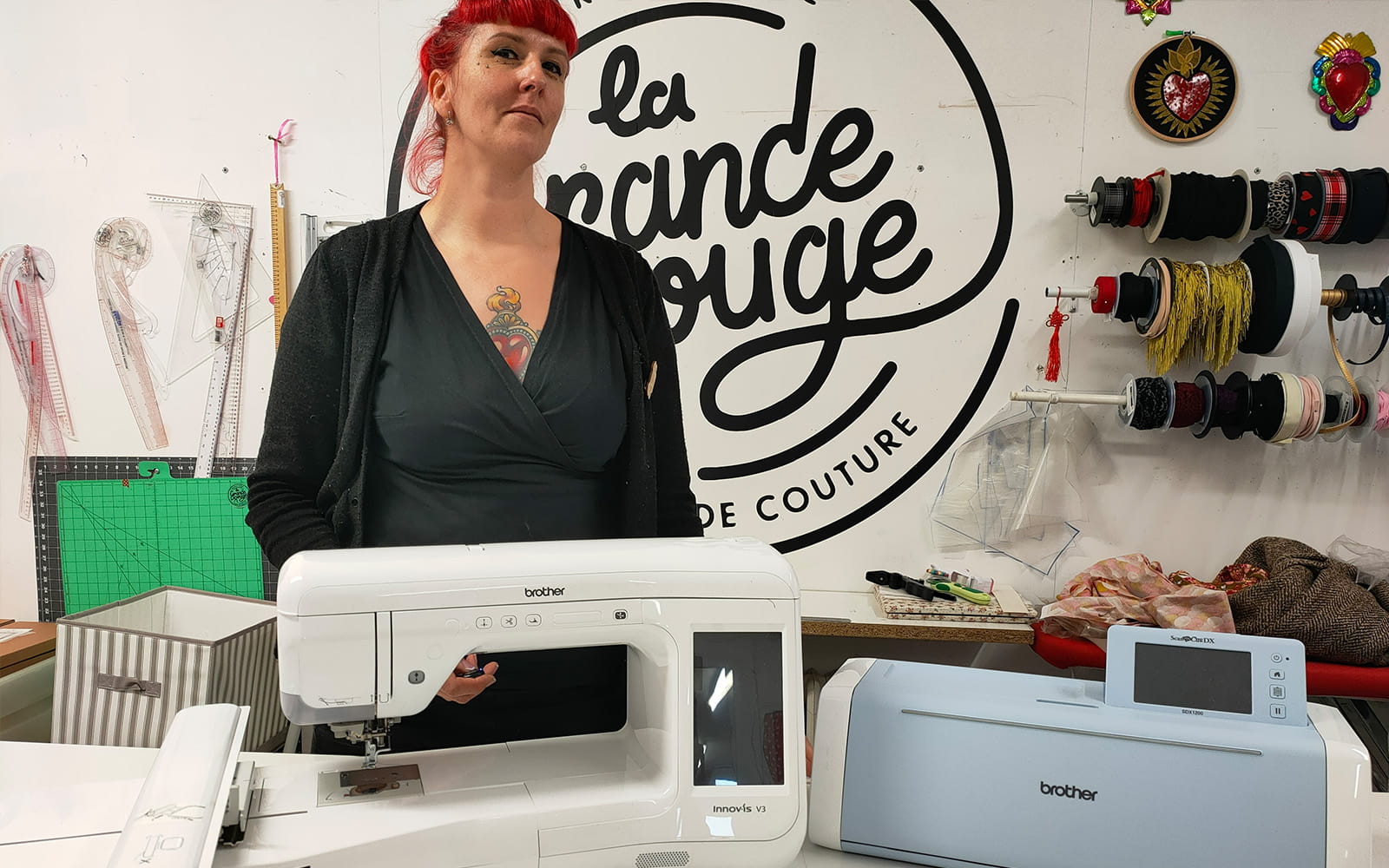 A red headed woman stands behind a sewing machine