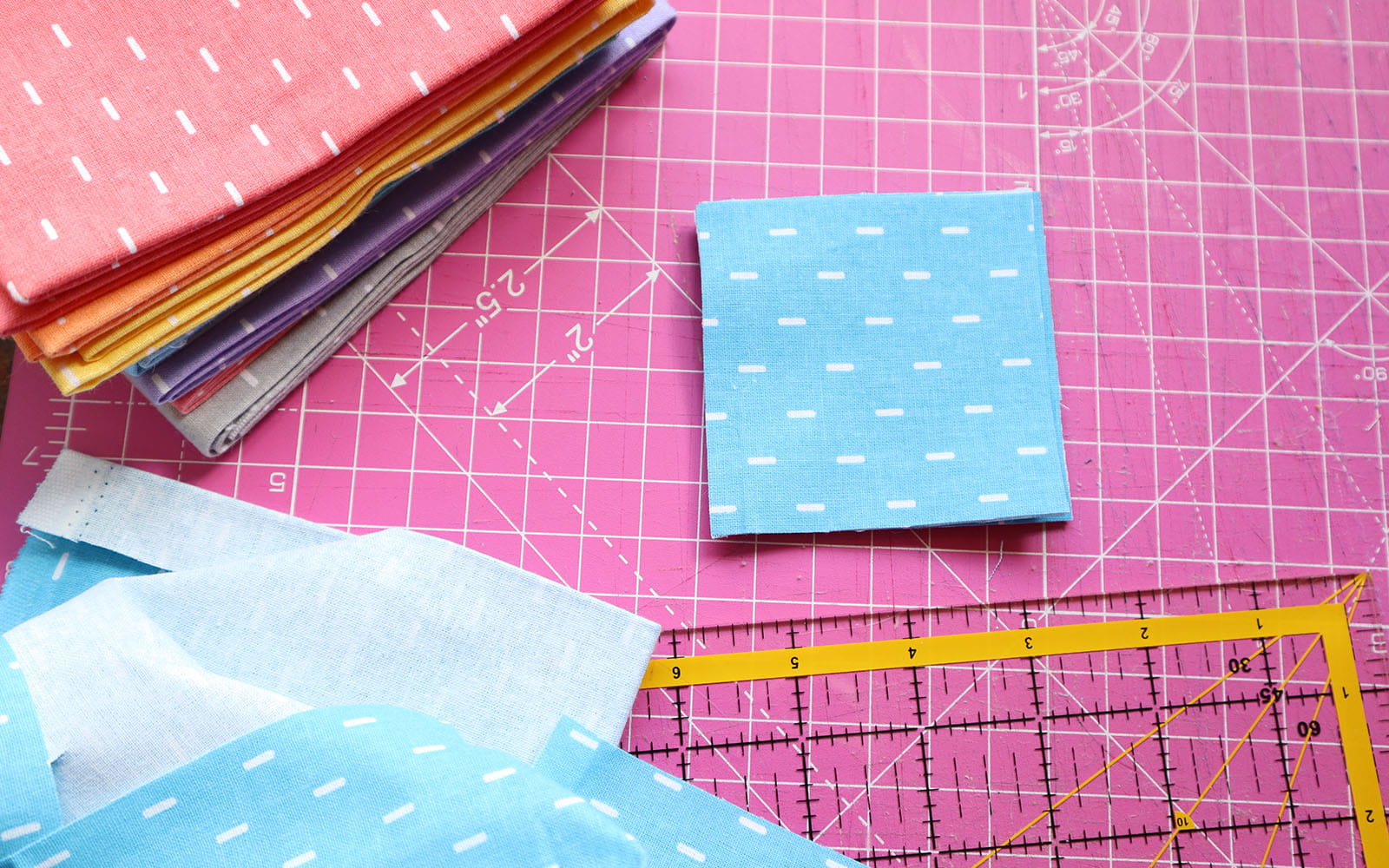 Stack of cut blue squares on pink cutting mat