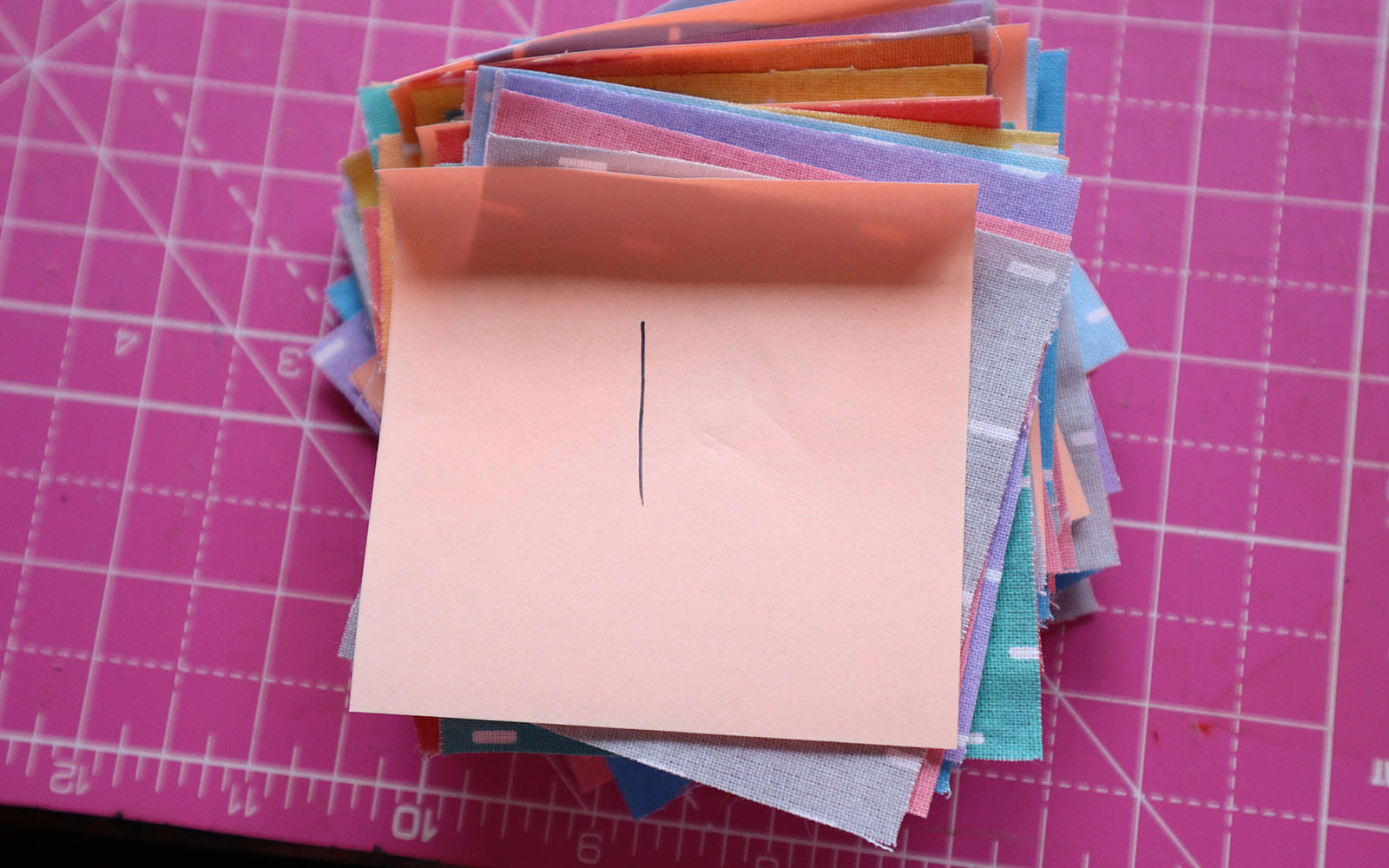 Pile of fabric squares in different colours on pink cutting mat