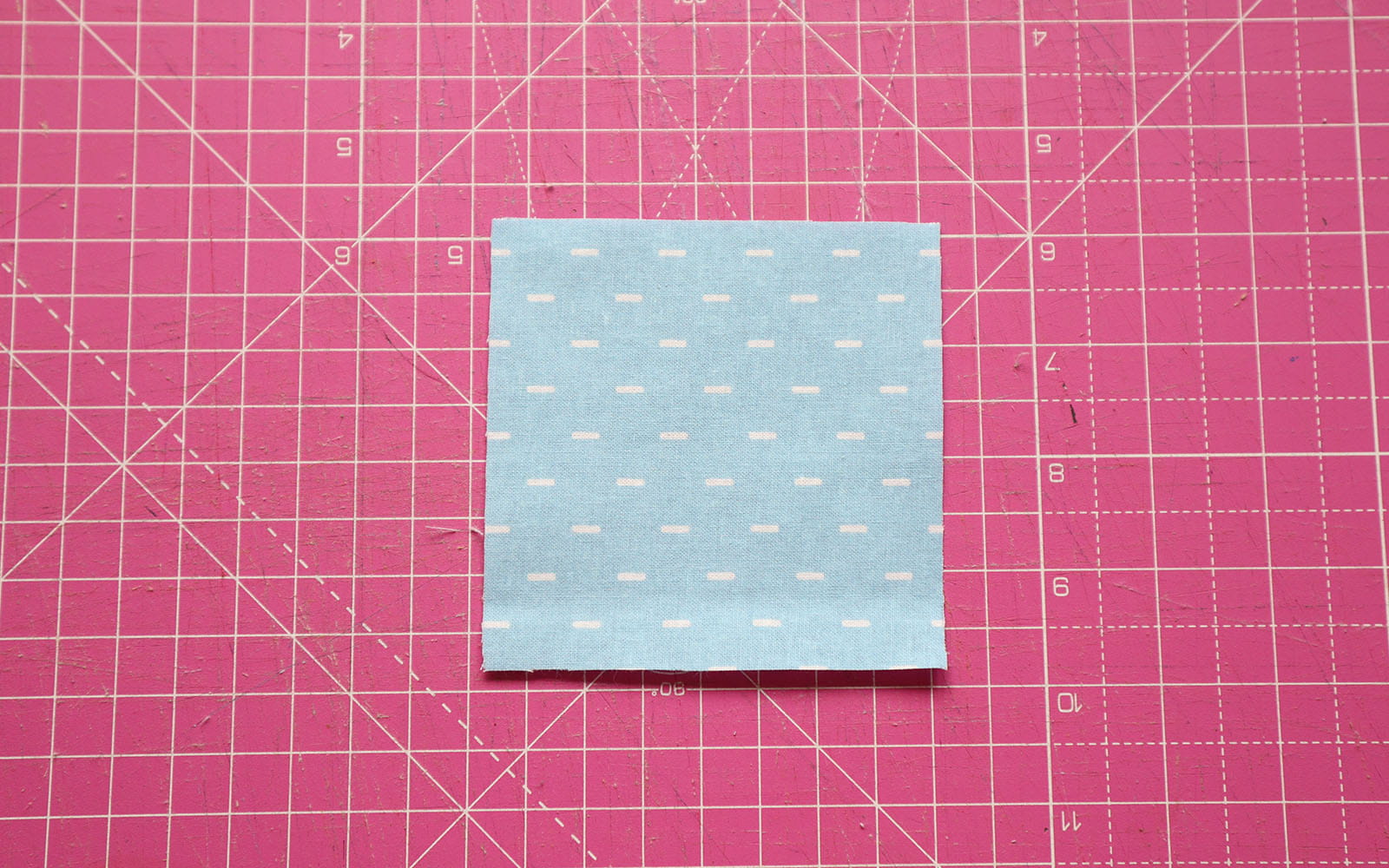 Blue fabric square on pink cutting mat