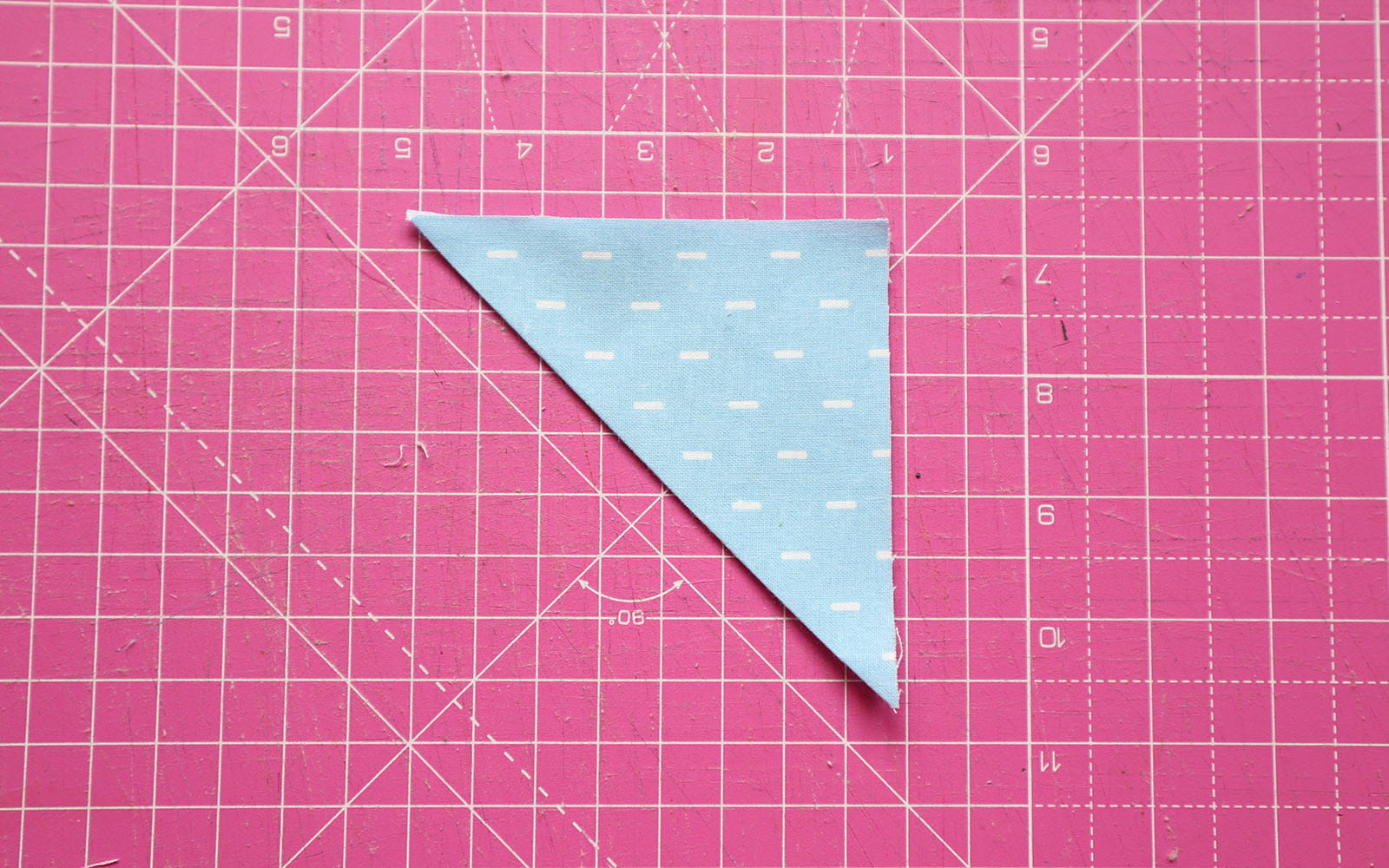Triangle shaped folded blue fabric on pink cutting mat