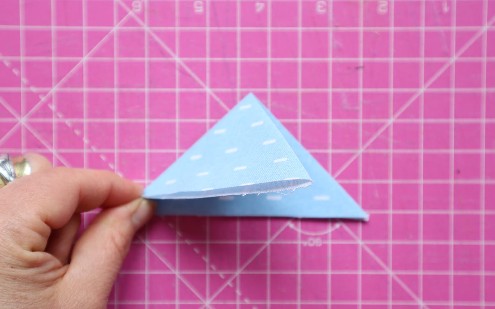 Hand holding double folded triangle blue fabric on pink cutting mat