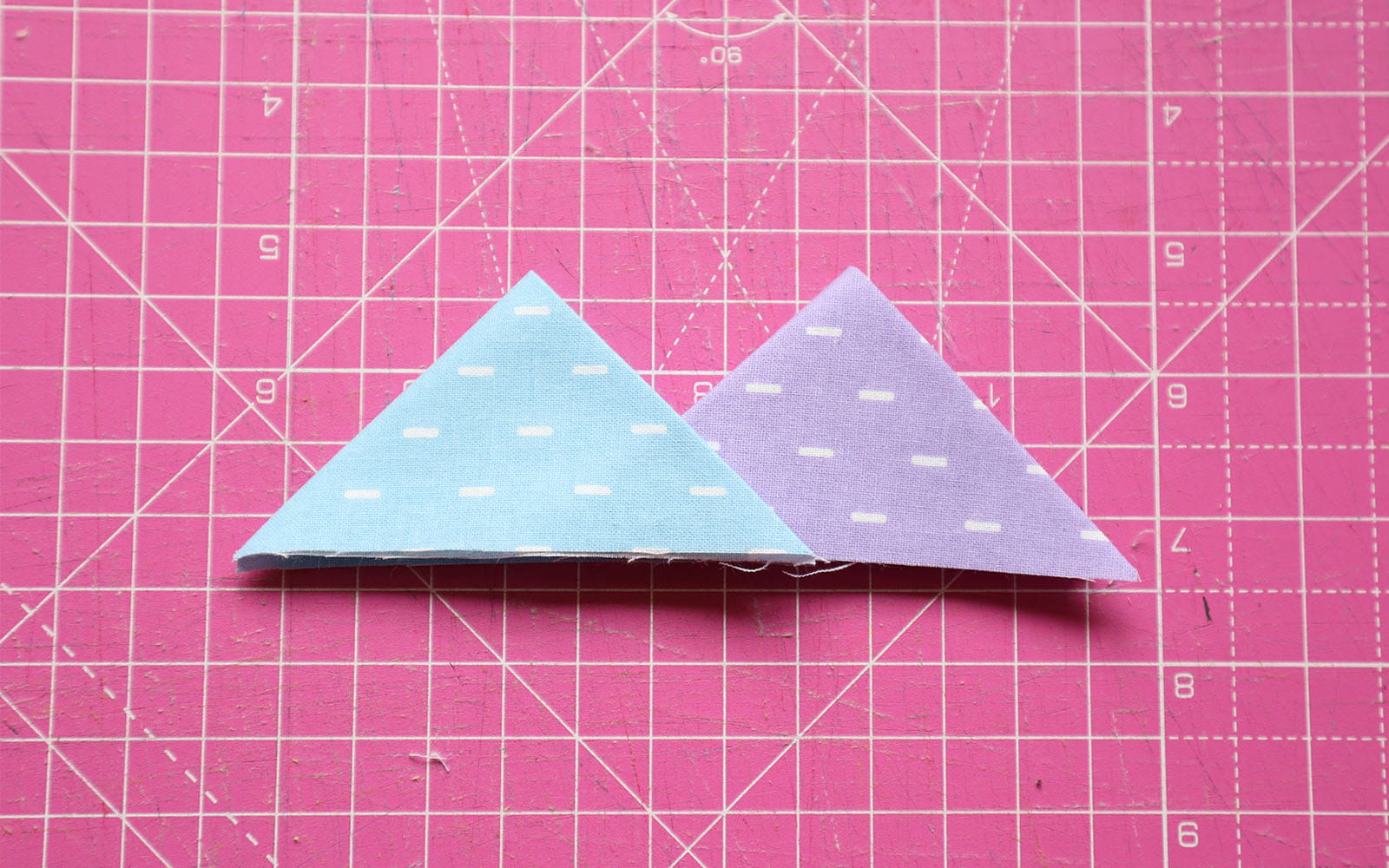 Blue and purple double folded fabric triangles on pink cutting mat