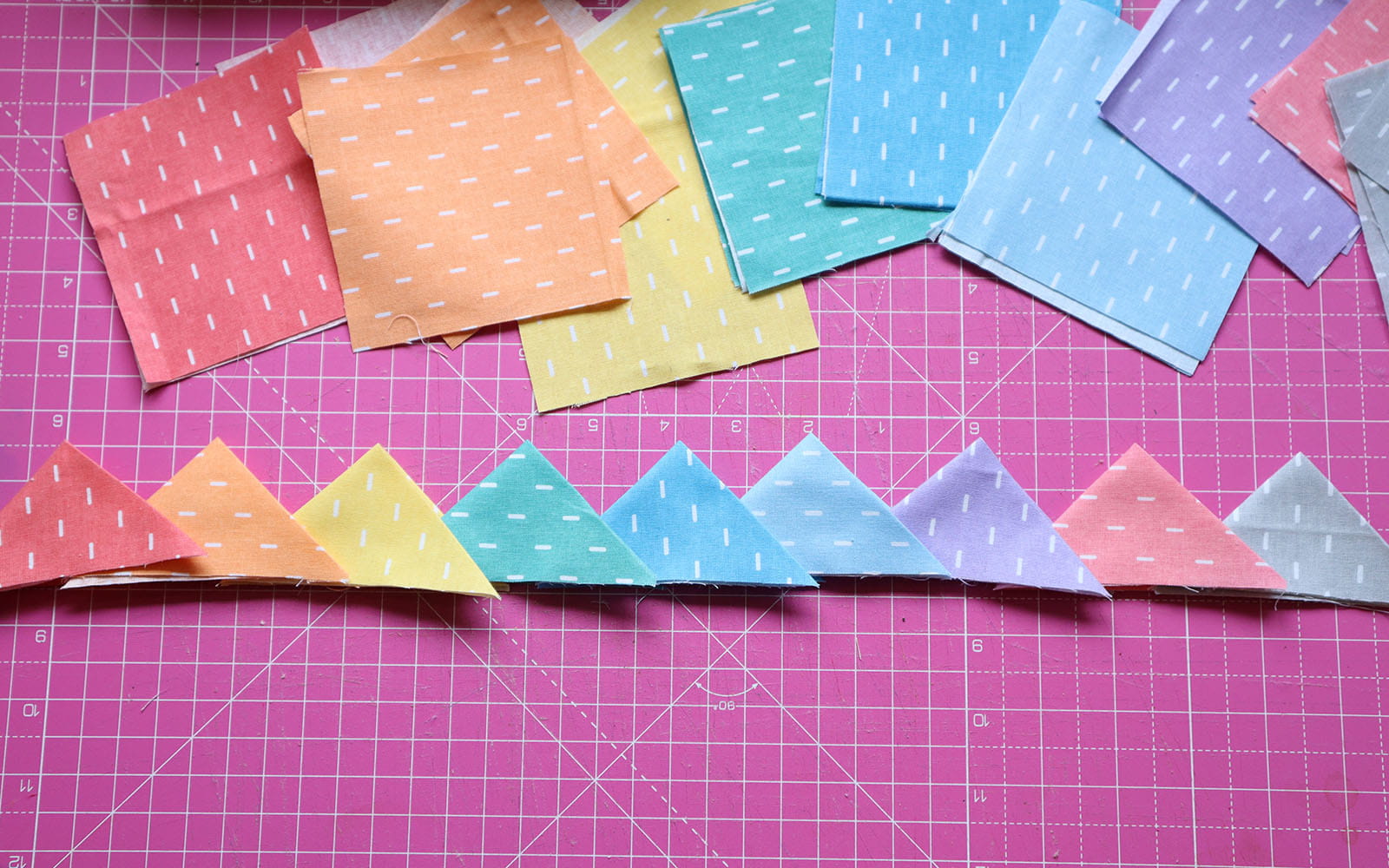 Row of fabric triangles and squares on pink cutting mat