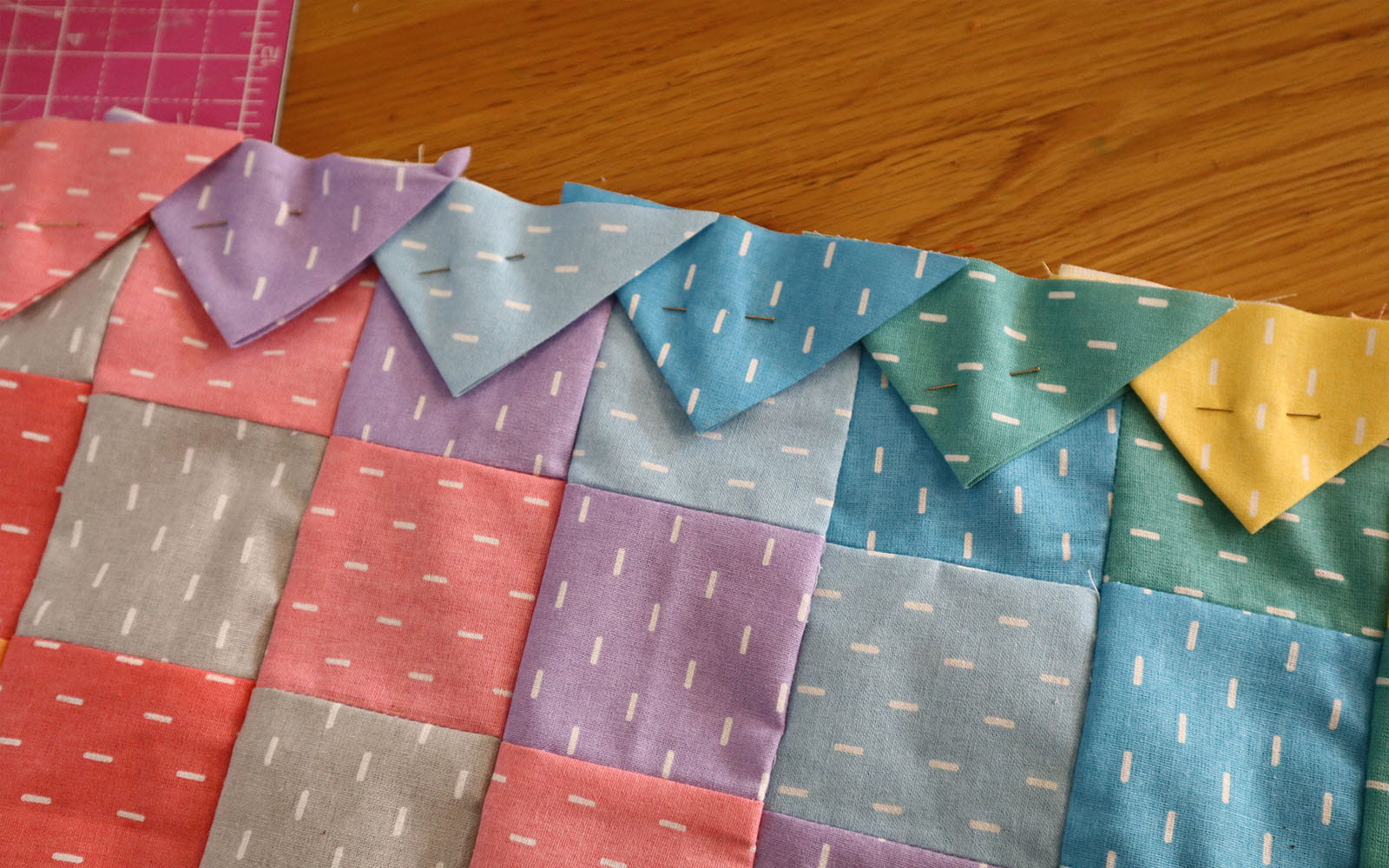 Fabric triangles pinned to edge of square pieced fabric