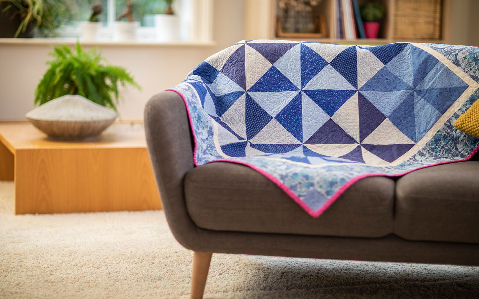 triangle blocked blue quilt with pink edge on grey sofa