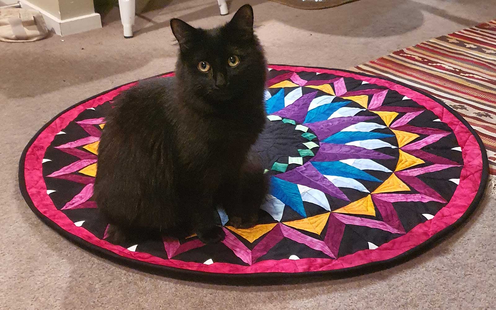 Schwarze Katze sitzt auf dem Kaleidoskop-Mandala-Quilt