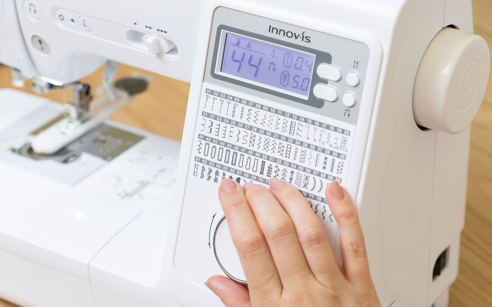 Hand on jog dial choosing sewing stitch on sewing machine