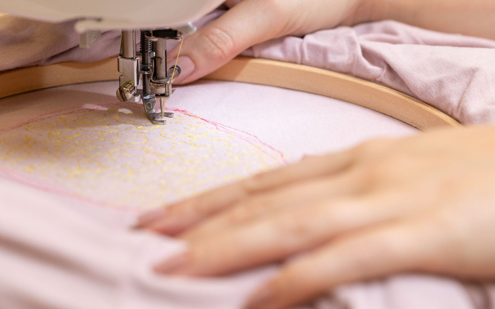 Hands holding wooden embroidery hoop stitching on sewing machine