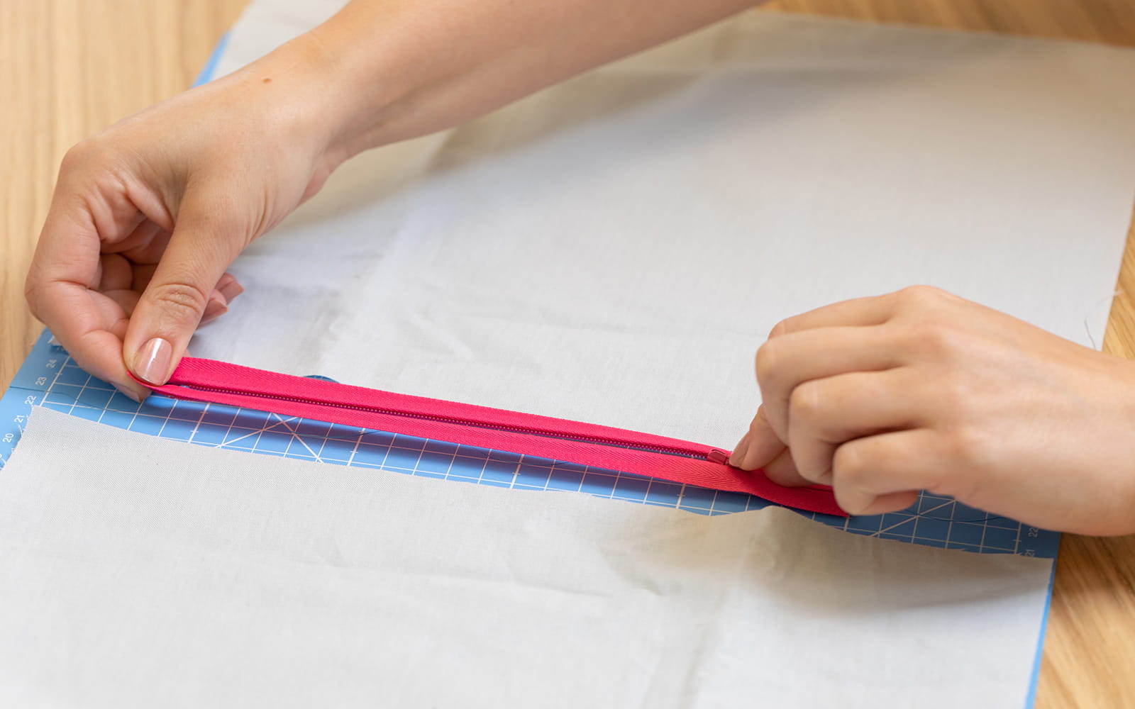 Hands pulling pink zipper open on blue cutting mat