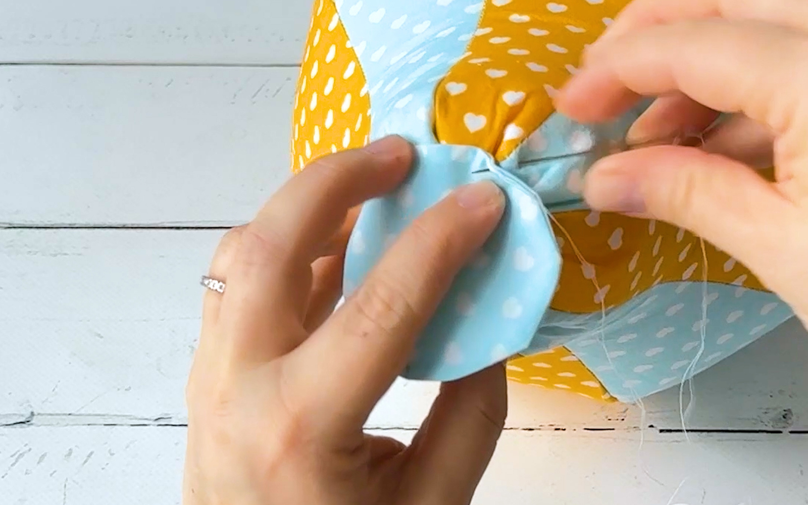 Fabric circle being sewn to bottom of fabric balloon with needle and thread.