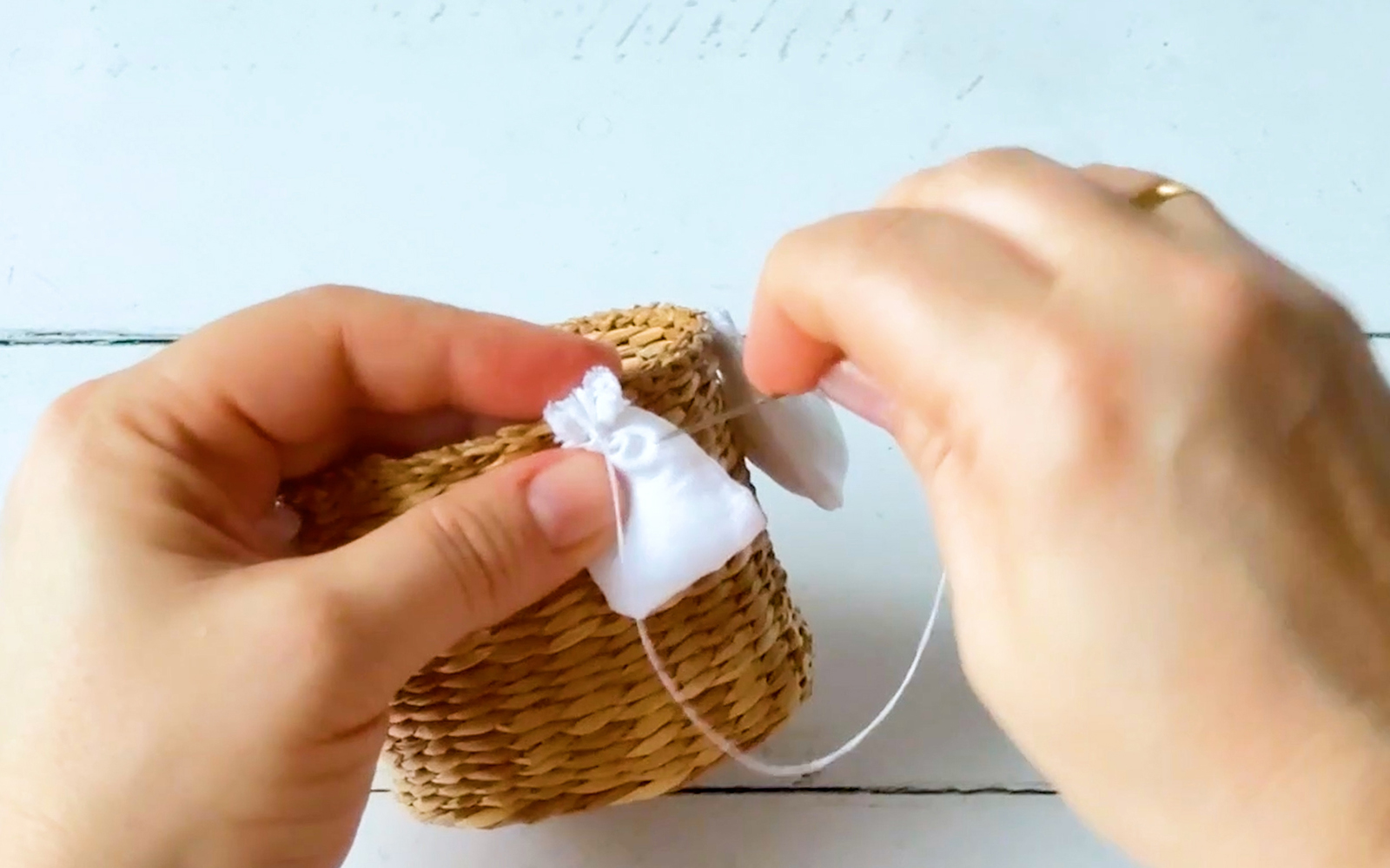 Hands sewing a small white bag to a basket