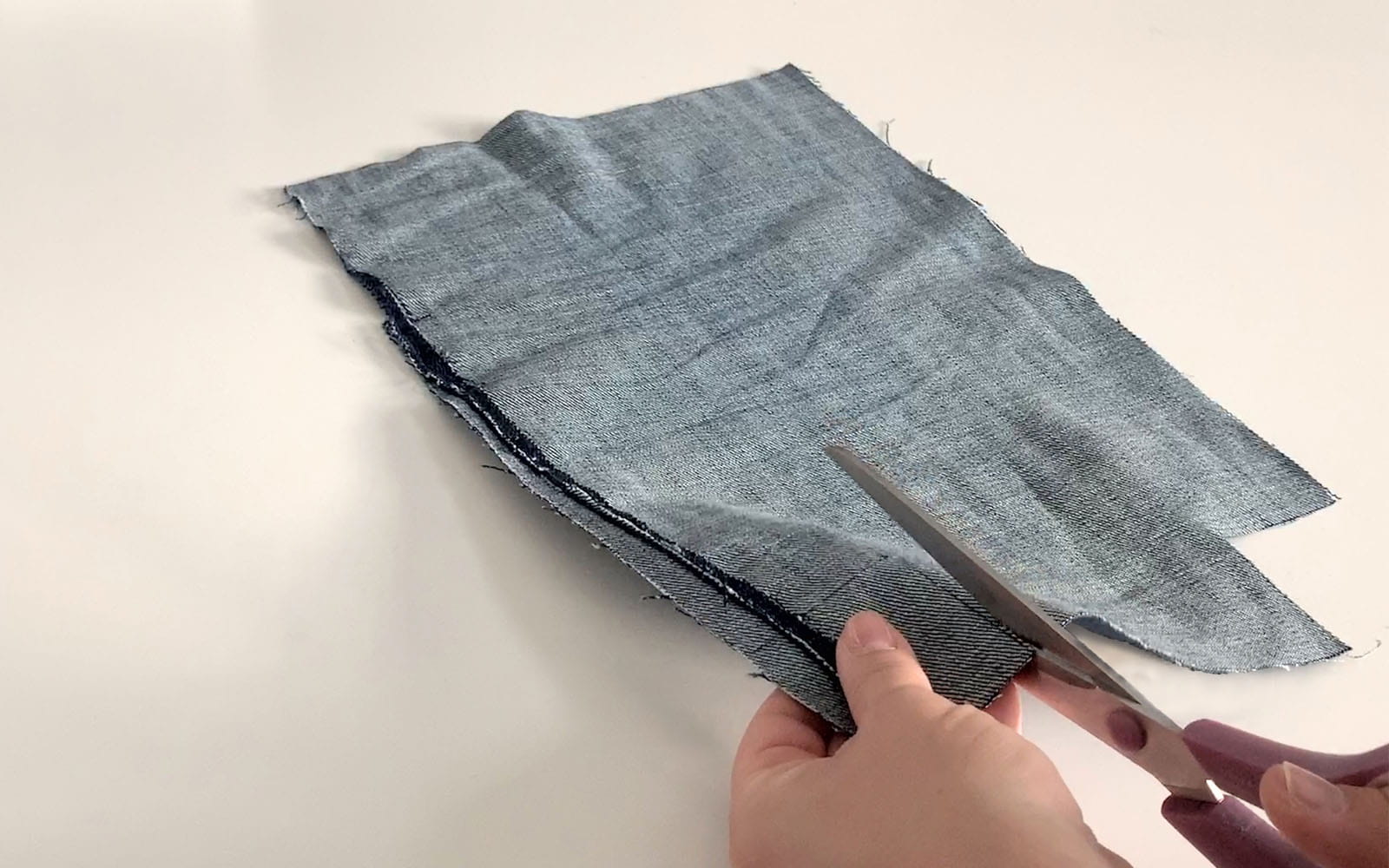 Hand holding scissors cutting small piece out of denim