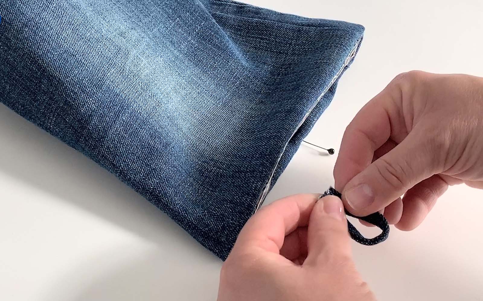 hand making small loop out of denim to attach to denim bag