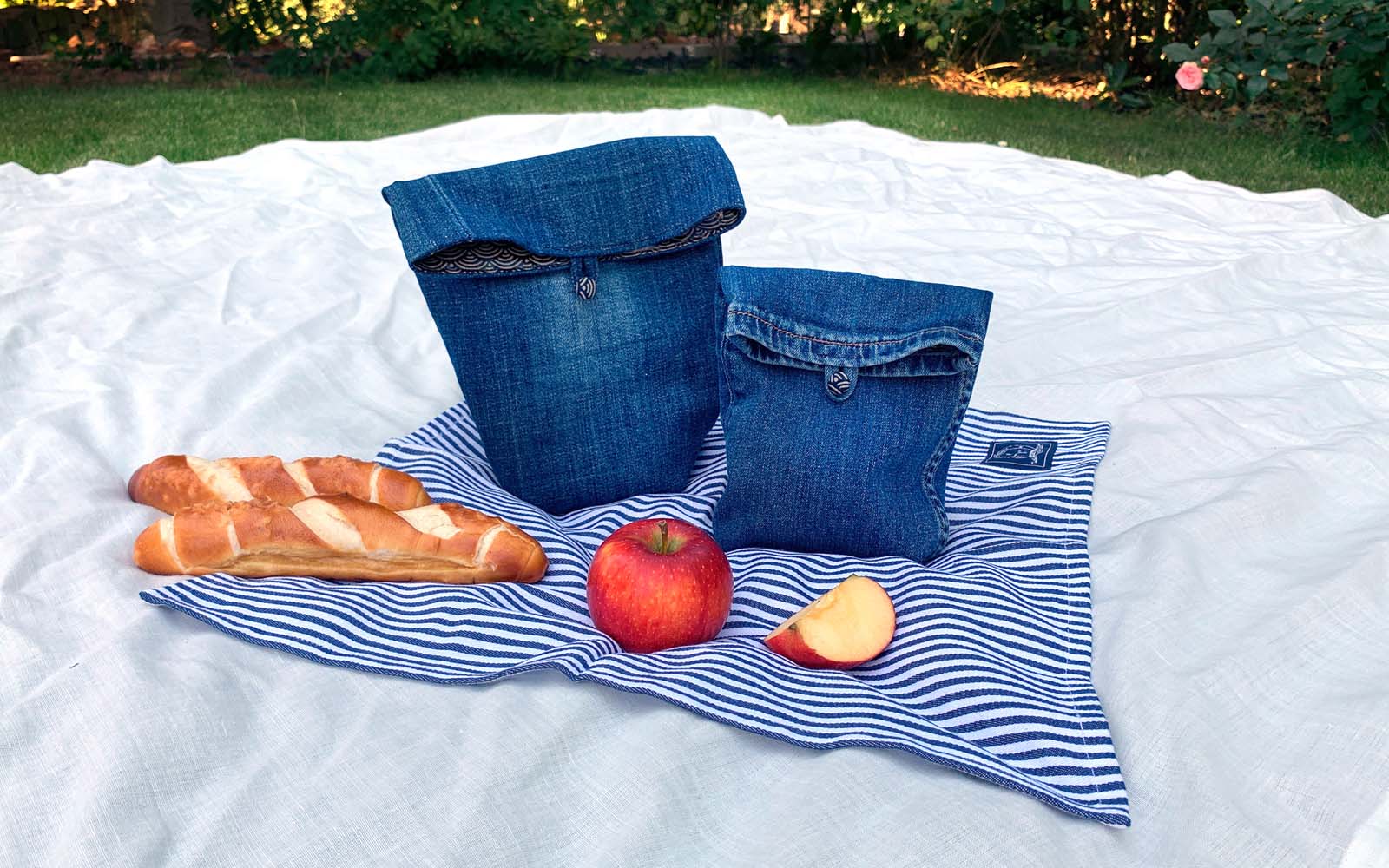 white picnic blanket blue striped napkin baguette and denim bag