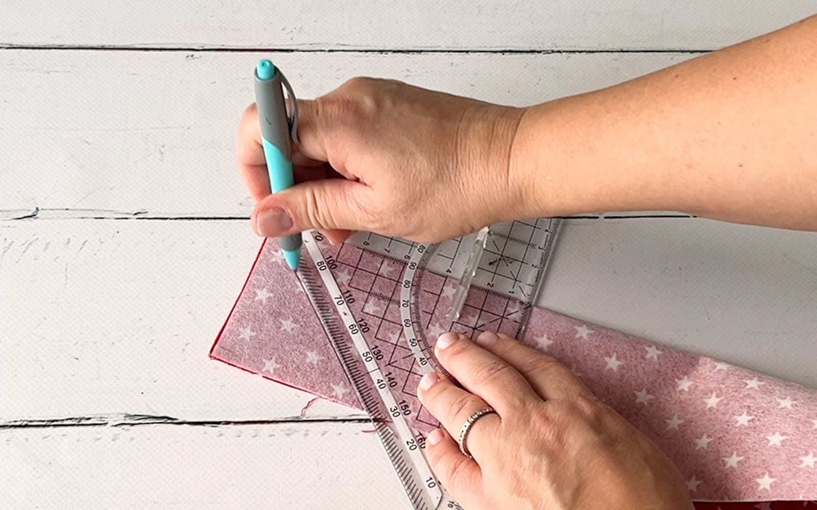 hand drawing a line on red fabric with triangle sewing ruler