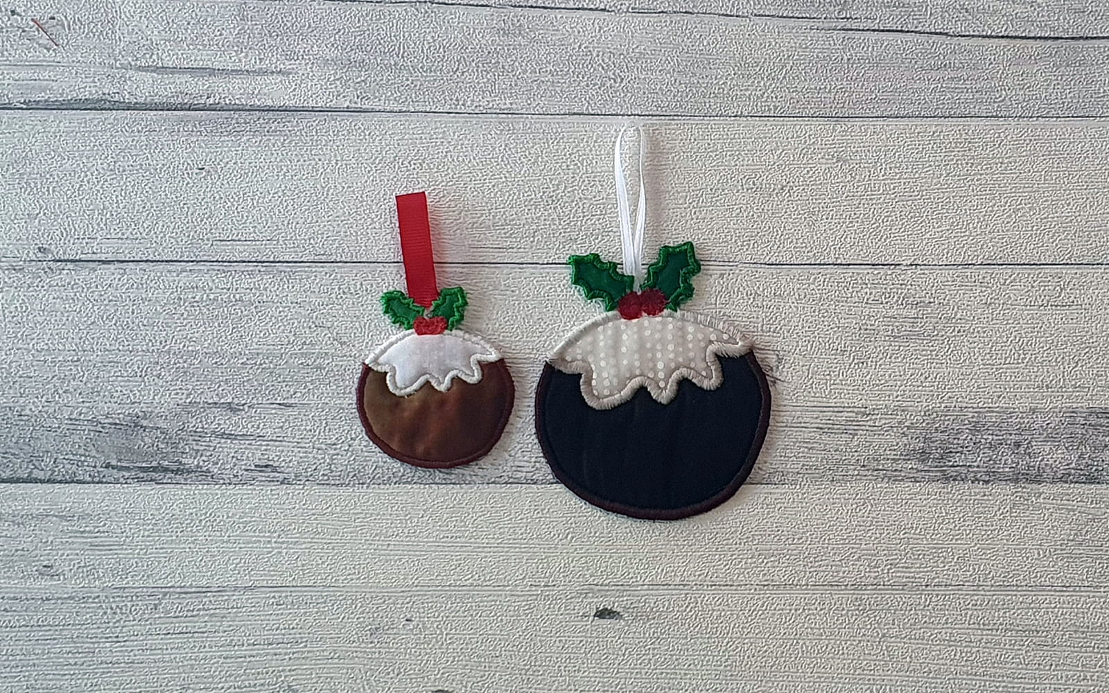 Two Christmas pudding ornaments on white wooden background