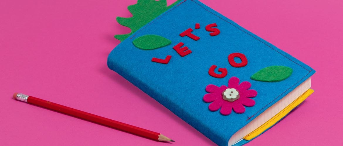 Blue felt book cover saying Let’s Go for notebook on pink background