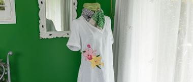 Weißes Leinenkleid mit Orchideenstickerei auf Mannequin gegen grüne Wand