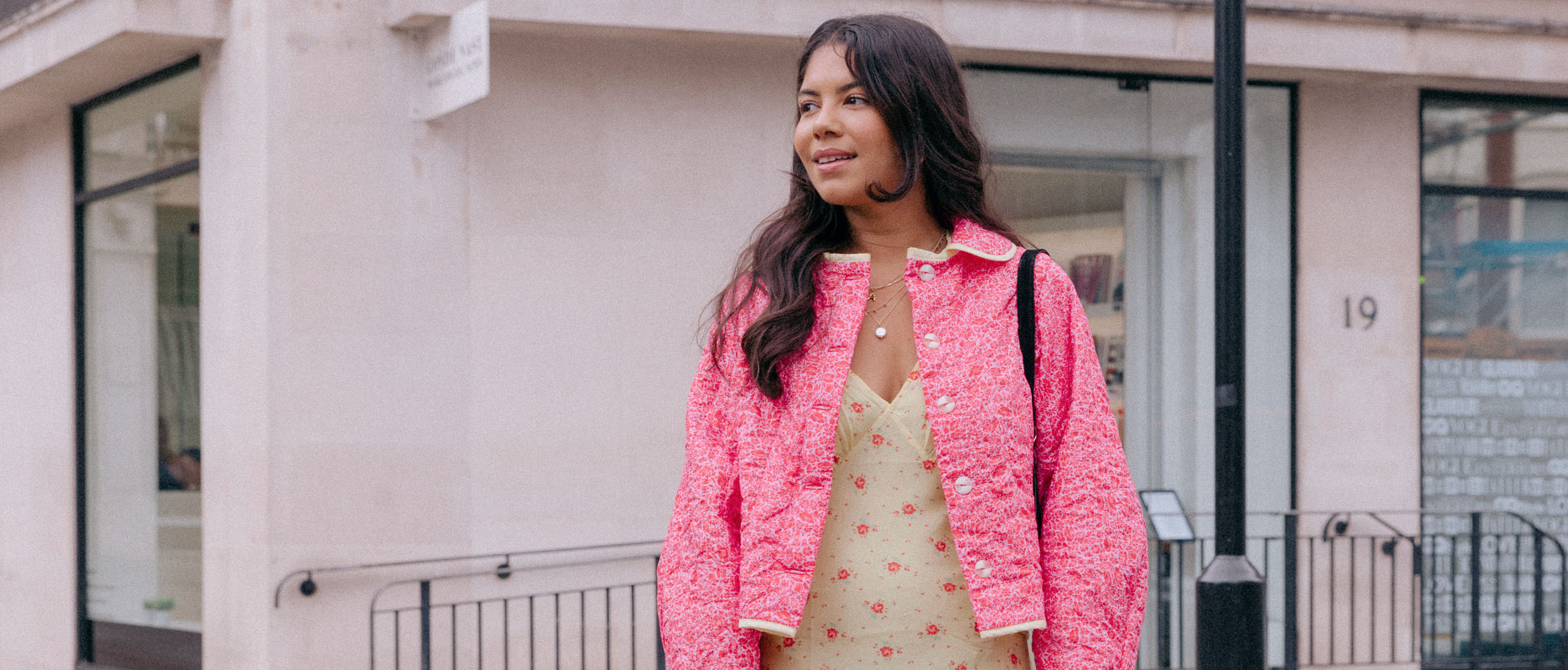 Woman in dress and pink jacket in front of a house wall