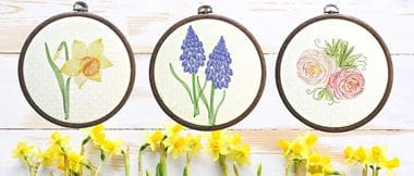 Embroidered flowers in round frames on wooden background.