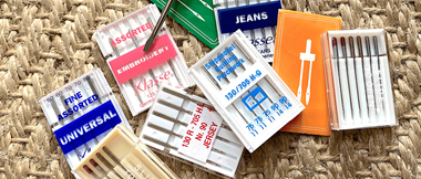 close up of assorted sewing machine needle packets on a woven background