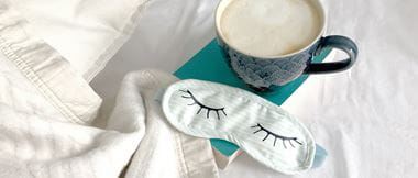 light green sleep mask with white blanket and blue mug with coffee