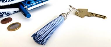 Blue metallic tasselled keyring with key next to open blue purse