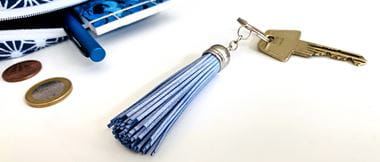 Porte-clés bleu métallique à glands avec clé à côté d'un sac à main bleu ouvert