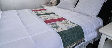 Bestickter Bettläufer mit Distelmuster auf weißer Bettdecke