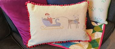 Cushion with senta and rudolpd embroidery and colorful quilt on sofa