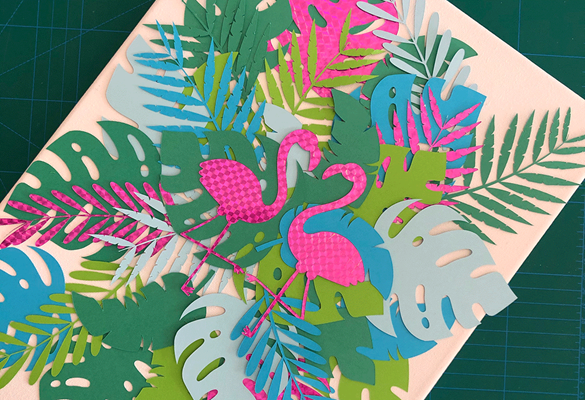 Two pink paper flamingos on colourful large green paper leaves