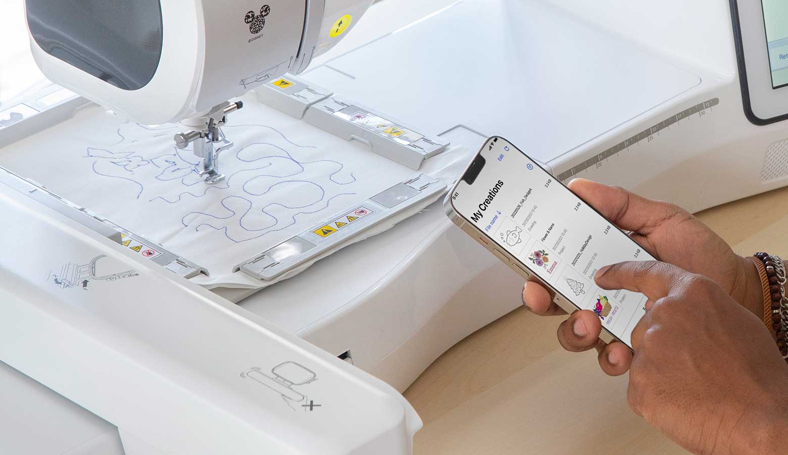 Smartphone with Brother Artspira app in front of embroidery machine