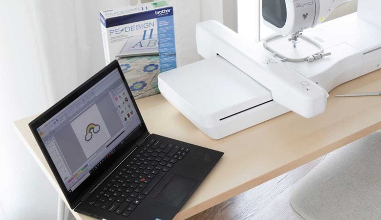 Laptop mit PE-Design läuft neben Nähmaschine auf einem Tisch