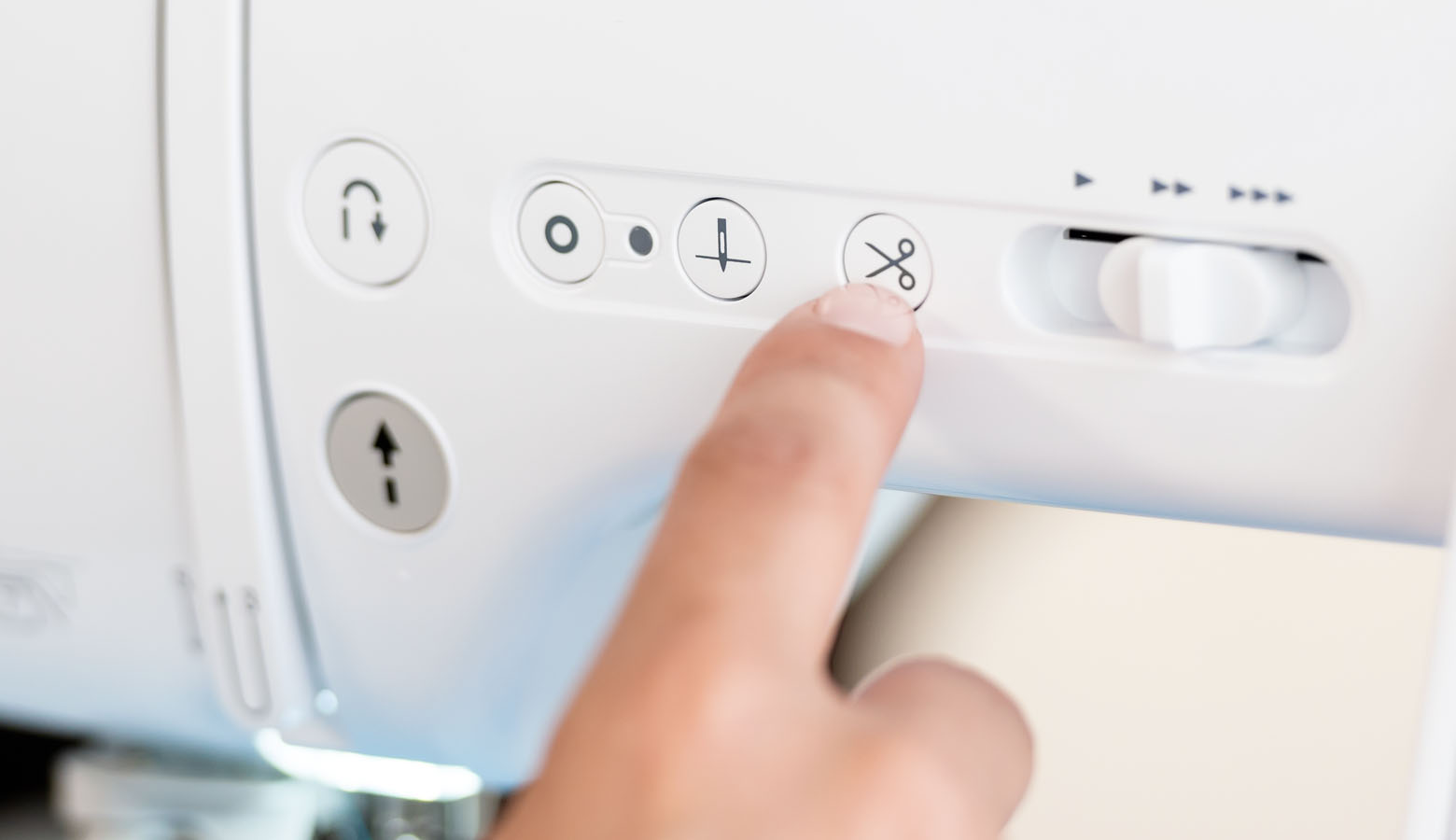 Finger drückt Fadenabschneiderknopf an Brother-Nähmaschine