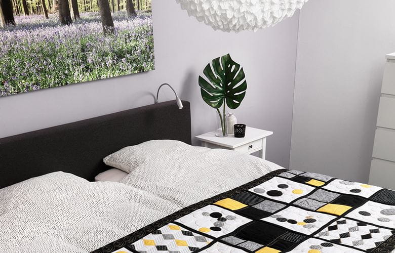 Zwart, geel en grijs dekbed op een bed in een lichte kamer