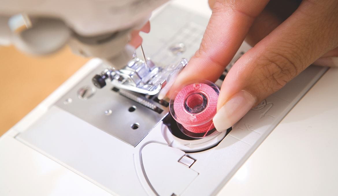 someone replacing the bobbin on a sewing machine