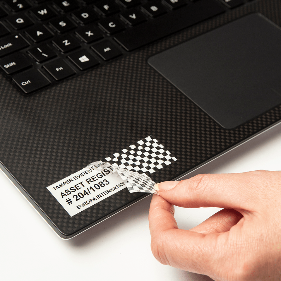 En person drar av en merkelapp på en bærbar datamaskin som er merket med en Brother P-touch TZeSE5 sort på hvit 24 mm bred sikkerhetstape